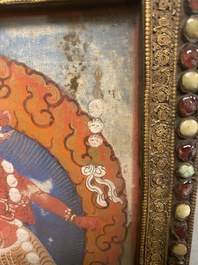 A Tibetan thangka in inlaid gilt brass frame, 19th C.